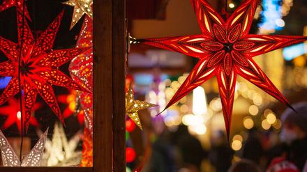 Eine Familie geht auf einem Weihnachtsmarkt an einem Marktstand mit leuchtenden Sternen vorbei.