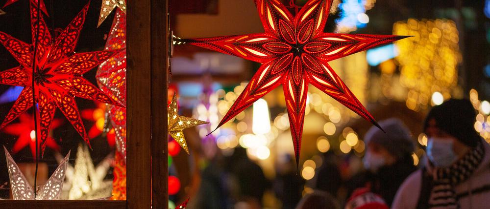 Eine Familie geht auf einem Weihnachtsmarkt an einem Marktstand mit leuchtenden Sternen vorbei.