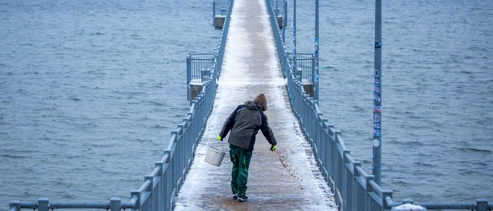 Auf der Seebrücke von Wismar wird die Schneedecke mit Sand abgestreut.