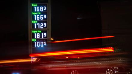 Autos fahren an einer Tankstelle vorbei, an der die Kraftstoffpreise angezeigt sind.
