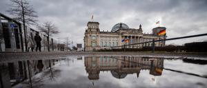 Das Reichstagsgebäude spiegelt sich am Morgen in einer Pfütze.