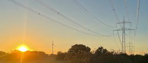 Strommasten stehen im Bucher Forst neben einem Windrad im Sonnenuntergang. 