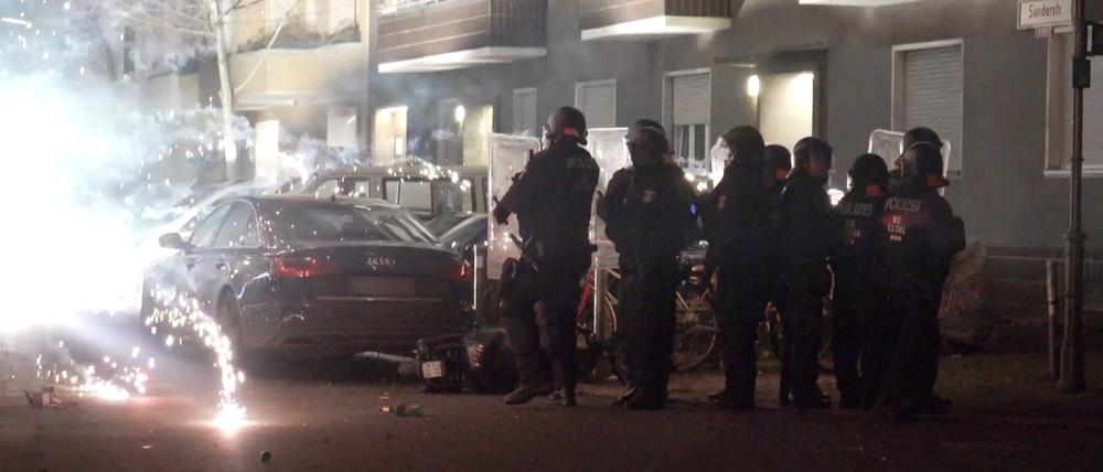 Polizisten stehen in der Silvesternacht 2022 hinter explodierendem Feuerwerk.