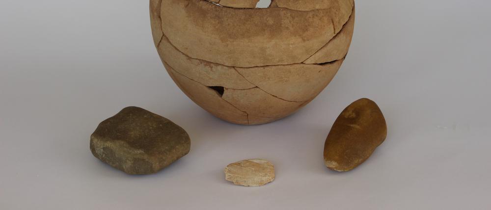 Der Krug aus der jordanischen Wüste enthielt ein Bruchstück eines Mahlsteins („Läufer“, links) eine Muschelschale aus dem Euphrat (Mitte) und einen bearbeiteten Kieselstein (rechts). 
