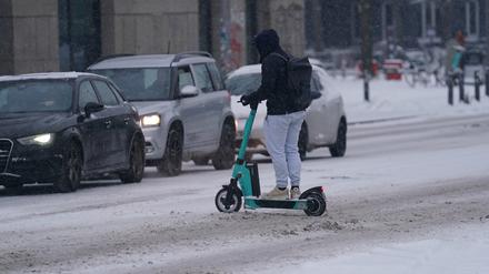 Ein Mann fährt mit einem E-Scooter über eine verschneite Straße. (Symbolbild)