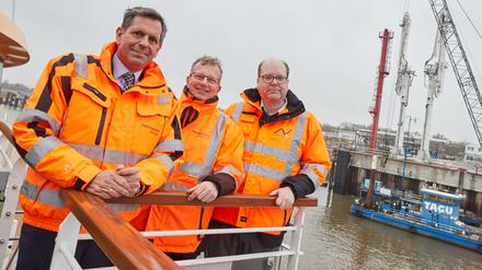 Olaf Lies (SPD), Holger Banik und Christian Meyer (Die Grünen) stehen auf der MS Helgoland. Im Hintergrund ist der Anleger für verflüssigte Gase (AVG) mit seinen Gas-Löscharmen zu sehen. 