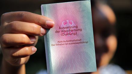 Eine junge Frau hält ihre Duldung in die Kamera. Sie ist drei Jahre gültig, solange bis sie ihre Ausbildung beendet hat. Auf dem Dokument ist vermerkt: Kein Aufenthaltstitel! Der Inhaber ist ausreisepflichtig!