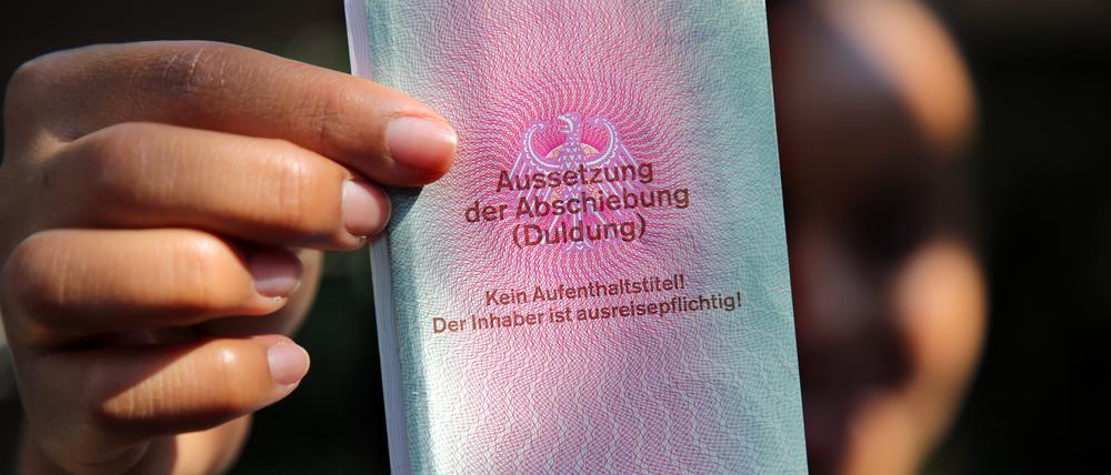 Eine junge Frau hält ihre Duldung in die Kamera. Sie ist drei Jahre gültig, solange bis sie ihre Ausbildung beendet hat. Auf dem Dokument ist vermerkt: Kein Aufenthaltstitel! Der Inhaber ist ausreisepflichtig!