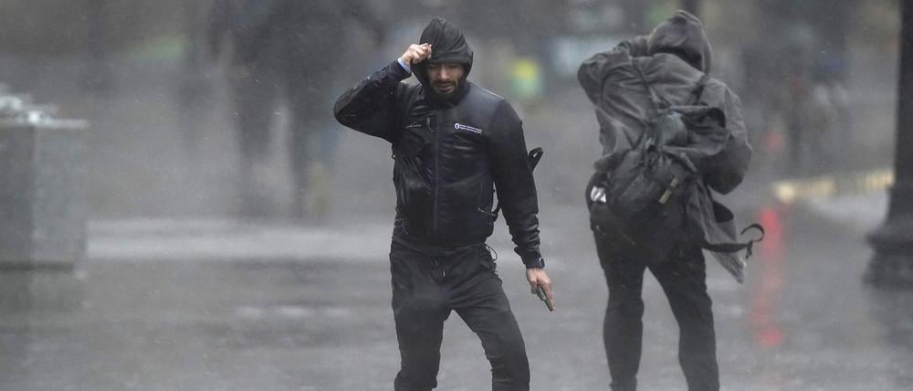 Menschen überqueren bei Wind und starkem Regen eine Straße. 