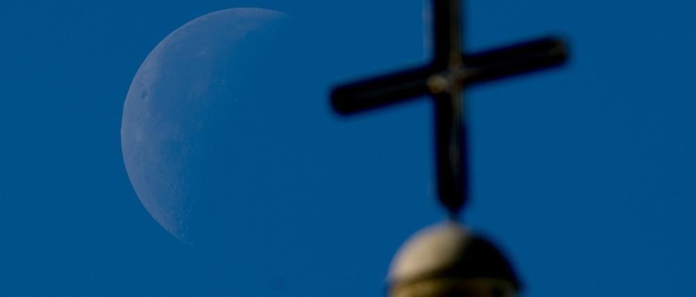 Abnehmender Mond hinter einem Kirchturm.