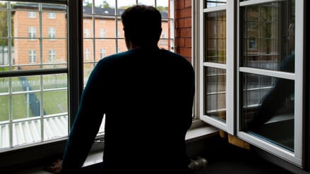 Ein Straftäter steht vor einem vergitterten Fenster in einer Klinik für Forensische Psychiatrie (Symbolbild)