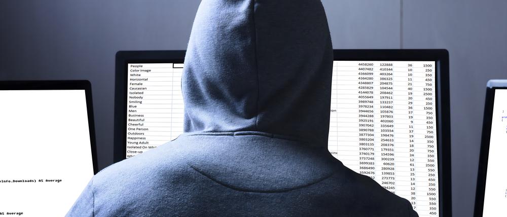 Rear View Of A Hacker Using Multiple Computers For Stealing Data On Desk