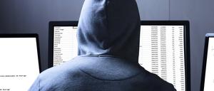 Rear View Of A Hacker Using Multiple Computers For Stealing Data On Desk
