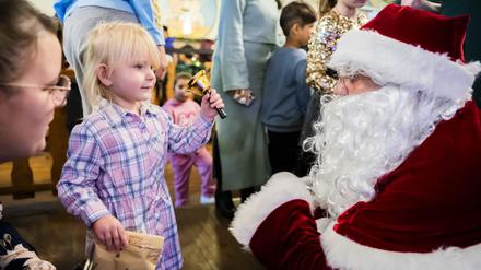 24.12.2023, Berlin: Die zweijährige Amelia-Marie läutet bei einem kostenlosen Weihnachtessen der Arche und des Hofbräus Berlin für Kinder und Familien aus benachteiligten Verhältnissen im Hofbräu Wirtshaus mit der Glocke des Weihnachtsmannes, nachdem sie von ihm ein Geschenk bekommen hat. Foto: Christoph Soeder/dpa - ACHTUNG: Nur zur redaktionellen Verwendung im Zusammenhang mit der aktuellen Berichterstattung über das genannte Thema und nur mit vollständiger Nennung des vorstehenden Credits +++ dpa-Bildfunk +++