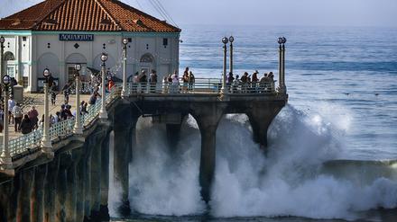 Menschen beobachten, wie die Brandung in Manhattan Beach in den USA an die Seite des Piers schlägt.