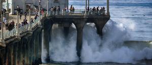 Menschen beobachten, wie die Brandung in Manhattan Beach in den USA an die Seite des Piers schlägt.