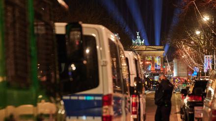 Polizeiwägen stehen unter den Linden, während Lichtstrahlen der Proben vor dem Brandenburger Tor darüber emporstrahlen. Die abendliche Party am Brandenburger Tor heißt ·Celebrate at the Gate· und startet um 20:15. Nach mehreren Jahren Pause gibt es wieder ein Höhenfeuerwerk. Laut Veranstalter könnten 65 000 Menschen kommen.