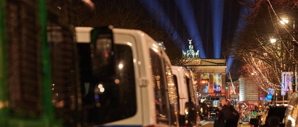 Polizeiwägen stehen unter den Linden, während Lichtstrahlen der Proben vor dem Brandenburger Tor darüber emporstrahlen. Die abendliche Party am Brandenburger Tor heißt ·Celebrate at the Gate· und startet um 20:15. Nach mehreren Jahren Pause gibt es wieder ein Höhenfeuerwerk. Laut Veranstalter könnten 65 000 Menschen kommen.