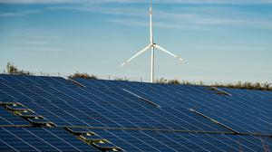 Ein Windrad steht auf einem Hügel oberhalb einer großflächigen Solaranlage auf einem Feld in Rheinland-Pfalz.
