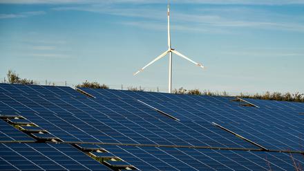 Ein Windrad steht auf einem Hügel oberhalb einer großflächigen Solaranlage auf einem Feld in Rheinland-Pfalz.