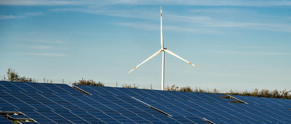 Ein Windrad steht auf einem Hügel oberhalb einer großflächigen Solaranlage auf einem Feld in Rheinland-Pfalz.