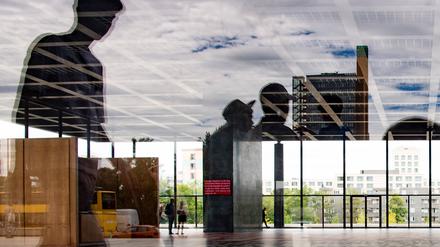 Besucher sind in der Halle der Neuen Nationalgalerie zu sehen, während sich Passanten in der Glasscheibe spiegeln. 