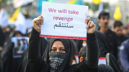 Eine Frau hält ein Schild mit der Aufschrift „Wir werden Rache ausüben“ hoch. 