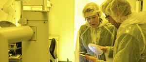 Wirtschaftssenatorin Franziska Giffey lässt sich vom technischen Leiter Arne Schleunitz die Produktion von Chips erklären. Das gelbe Licht im Reinraum schützt die Chemikalien.