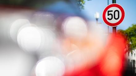 Ein Verkehrsschild zur Geschwindigkeitsbegrenzung auf Tempo 50 steht auf einer Hauptstraße vor geparkten Autos. 