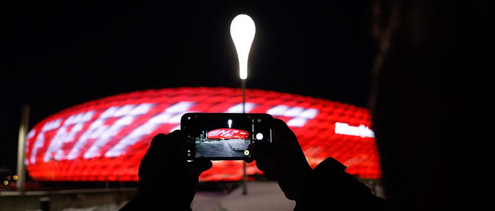 Eine Person fotografiert mit einem mobilen Gerät die Allianz Arena, das Stadion des FC Bayern, während die Worte „Danke Franz“ zu Ehren von Franz Beckenbauer auf die Arena projiziert werden.