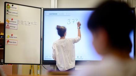Eine Lehrerin schreibt eine Mathematikaufgabe auf eine digitale Schultafel im Klassenraum einer 4. Grundschulklasse.