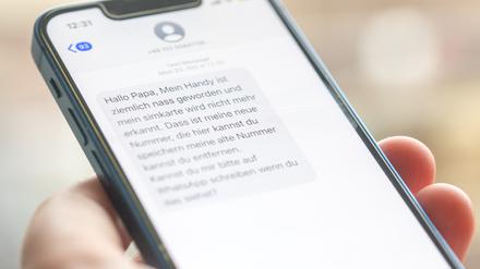 Eine Frau hält ein Smartphone in ihrer Hand, auf dessen Display eine Betrugs-SMS zu lesen ist. 