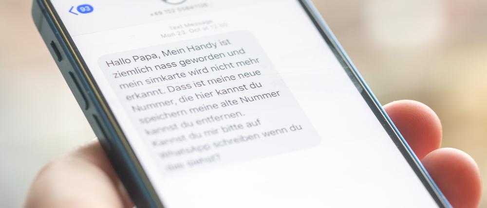 Eine Frau hält ein Smartphone in ihrer Hand, auf dessen Display eine Betrugs-SMS zu lesen ist.