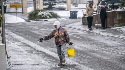Eine Frau verteilt Streusalz bei Regen und Schneeglätte auf einem Fußweg in Heilbronn.