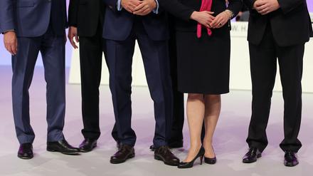 Mehrere männliche und ein weibliches Vorstandsmitglied stehen auf einer Hauptversammlung zusammen auf dem Podium. 