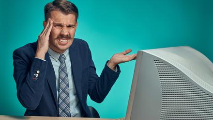 The sad, puzzled, disappointed young man in a business suit working on computer at desk on blue studio background