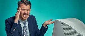 The sad, puzzled, disappointed young man in a business suit working on computer at desk on blue studio background