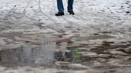 Ein Mann in Leipzig geht durch Schneematsch. In der Nacht stiegen die Temperaturen in die Plusgrade und es setzte Tauwetter ein. 