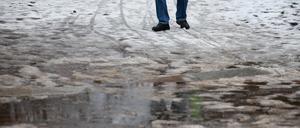Ein Mann in Leipzig geht durch Schneematsch. In der Nacht stiegen die Temperaturen in die Plusgrade und es setzte Tauwetter ein. 