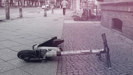 Ein E-Scooter liegt achtlos auf einem Grünstreifen an einer Straße. 