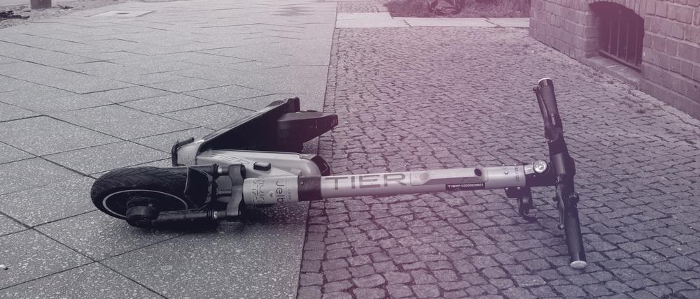 Ein E-Scooter liegt achtlos auf einem Grünstreifen an einer Straße. 