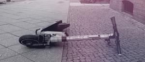 Ein E-Scooter liegt achtlos auf einem Grünstreifen an einer Straße. 