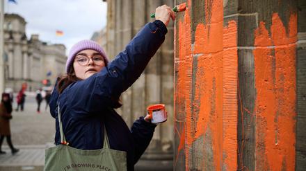 Eine Klimaaktivistin bemalt das Brandenburger Tor mit oranger Farbe.