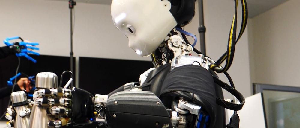 Der ferngesteuerte Roboter iCub3 hebt zwei Flaschen auf. 