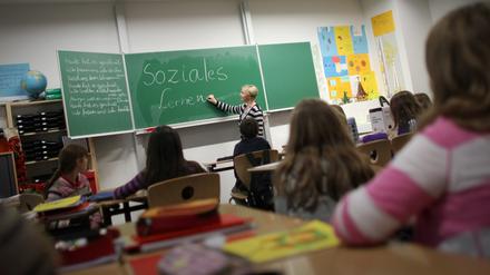 Eine Lehrerin schreibt in einer Klasse an der Tafel.