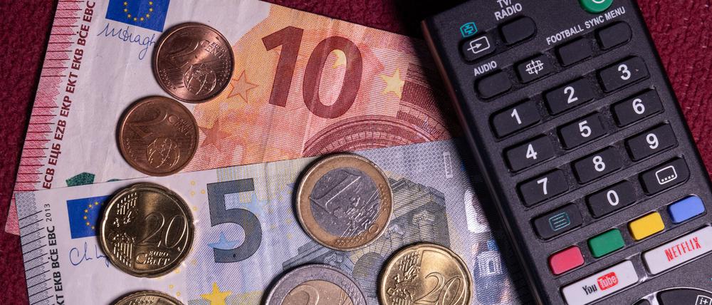 Die Summe von 18,94 Euro liegt auf einem Tisch neben der Fernbedienung für einen Fernseher. Der Rundfunkbeitrag soll ab 2025 vorläufigen Berechnungen von Finanzexperten zufolge um 58 Cent steigen.