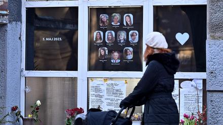 Eine Fußgängerin schiebt ihren Kinderwagen an der Schule in Belgrad vorbei, in der im Mai vergangenen Jahres ein 13-Jähriger neun Menschen erschoss. Im Fenster hängen Bild der Getöteten.