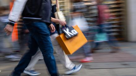 Menschen mit vollen Einkaufstaschen gehen an Geschäften vorbei. 