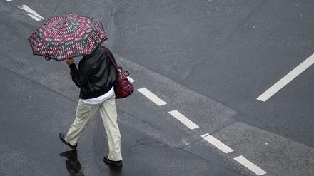Mit einem Schirm schützt sich eine Passantin in Frankfurt vor dem strömenden Regen (Symbolbild).