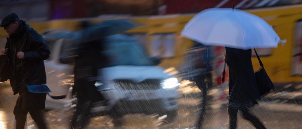 Passanten mit Regenschirmen gehen im Regen über die Straße.